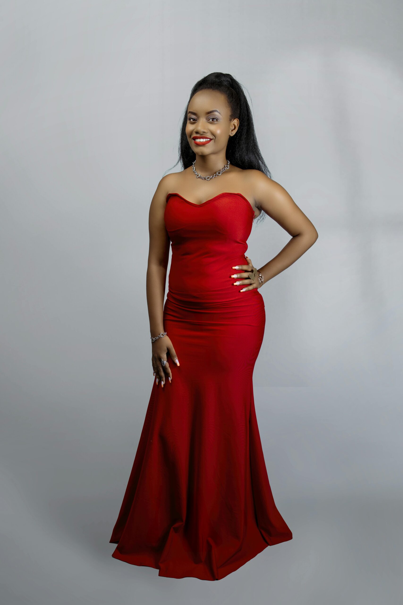 A beautiful African woman poses elegantly in a red evening gown. Studio portrait.